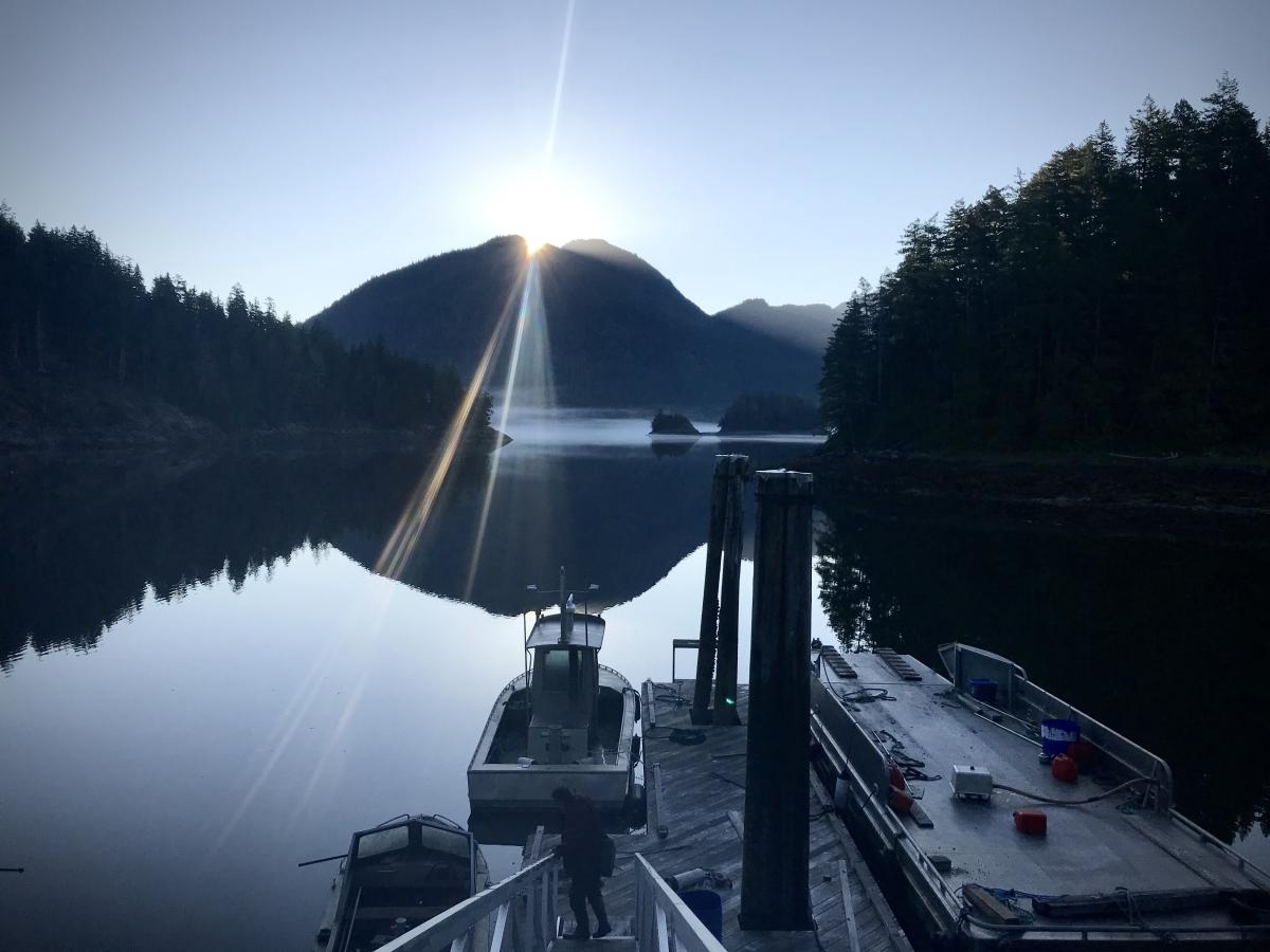 An early morning lake view with a dock and empty boat in the foreground and mountains in the background