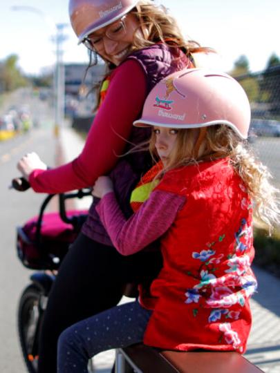 Woman and young girl wearing helmets on bicycle on street