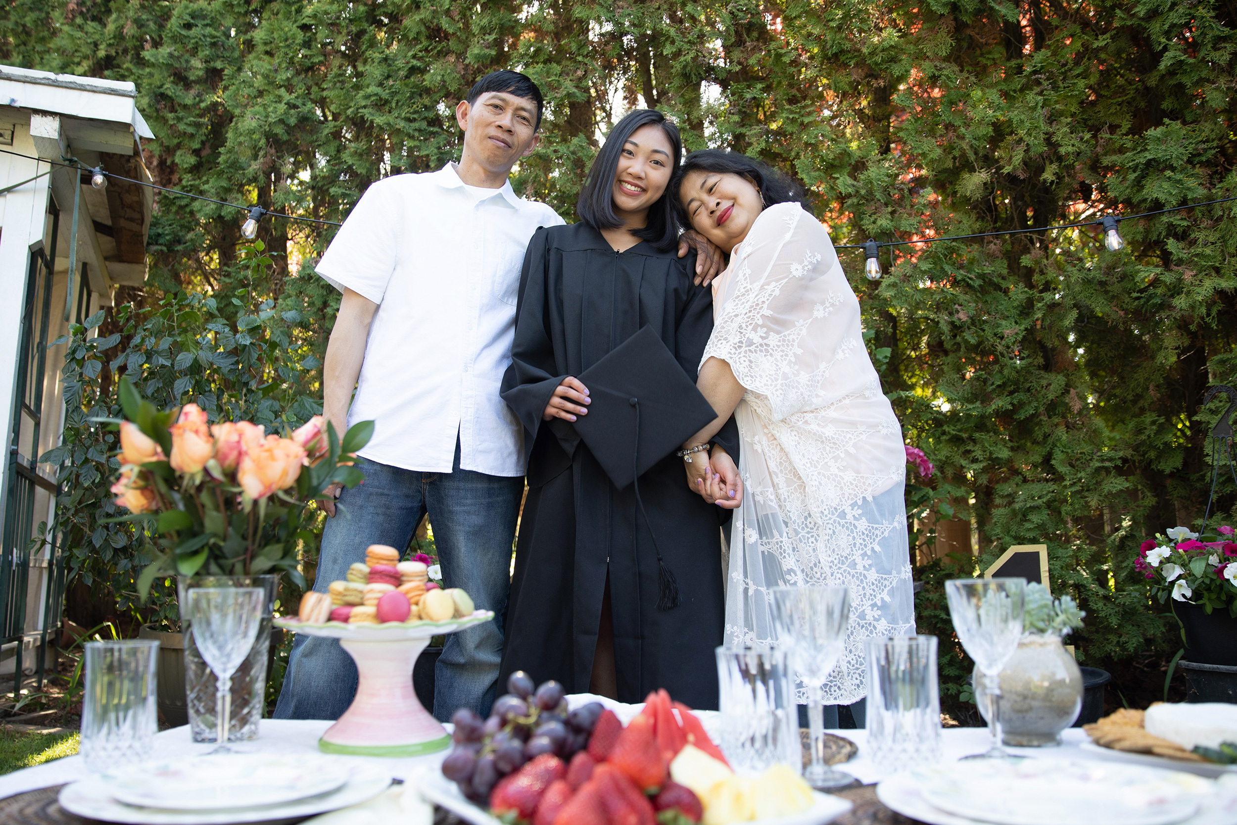 Student in graduation gown, posing with her parents at an outdoor celebration