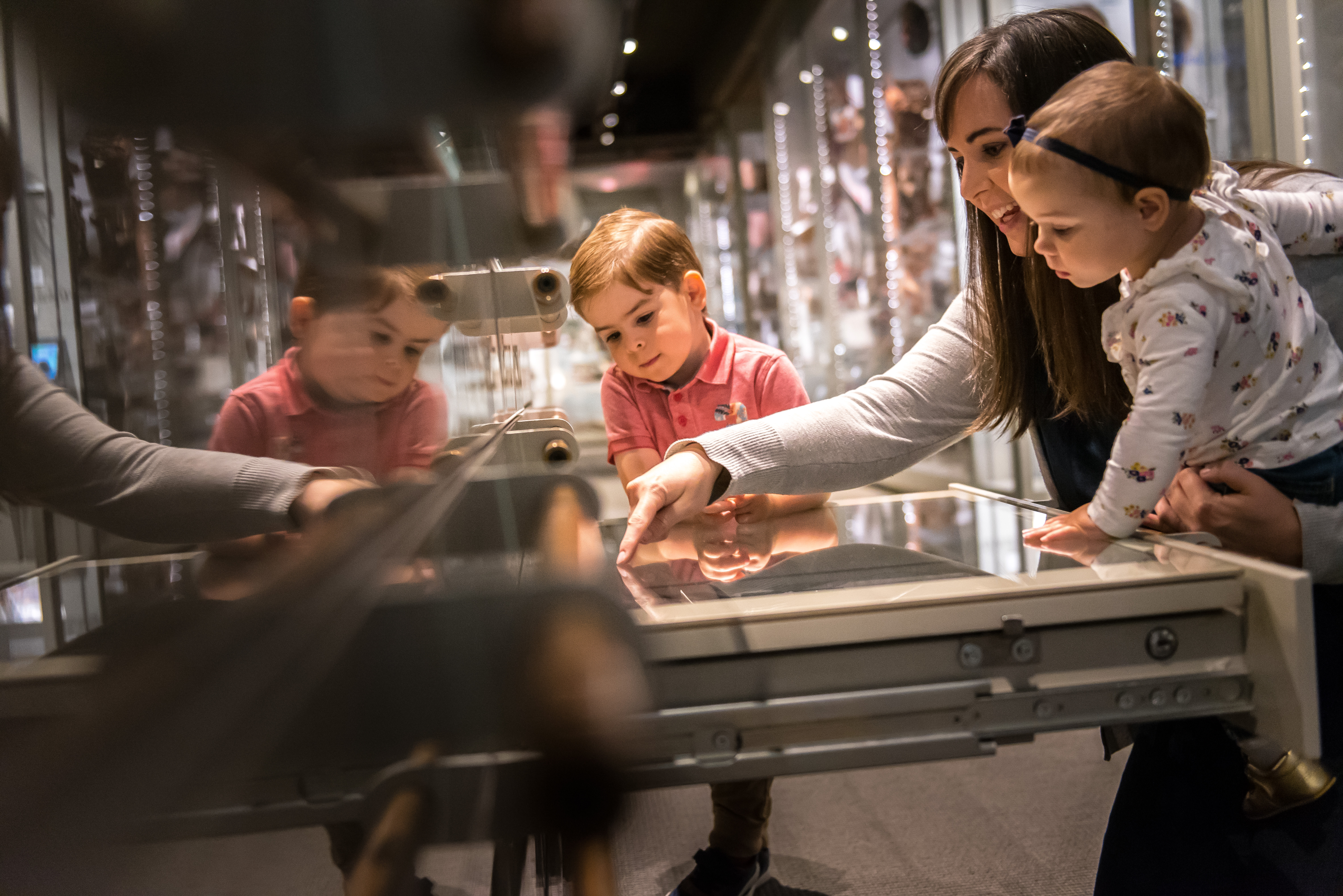 A mother with her two young children exploring a drawer of artifacts inside the Museum of Anthropology