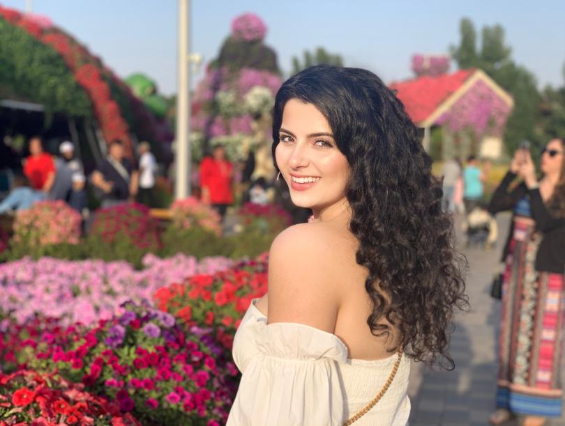 Leanne Rachid at the Dubai Miracle Garden, with lots of flowers in bloom in the background
