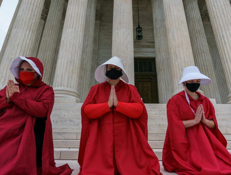 Women in red robes and white bonnets pray on steps in The Handmaid's Tale