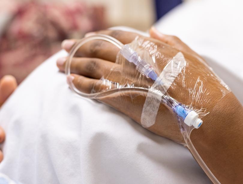 Patient in hospital with IV tube attached to hand holds pregnant stomach