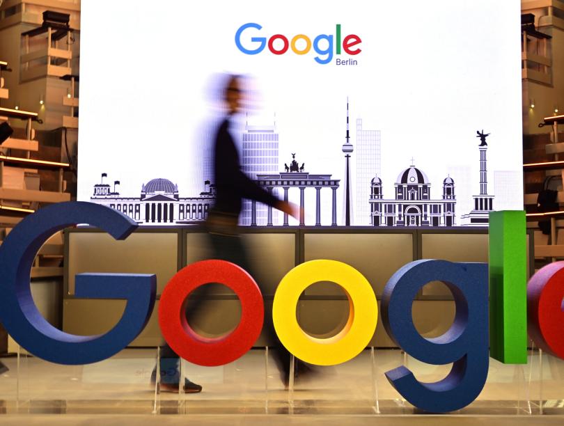 Man walks in front of screen and behind Google logo 