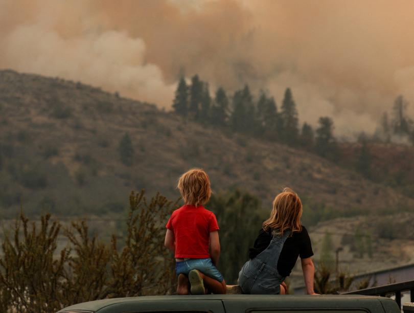The back of two children as they look at a wildfire in the distance