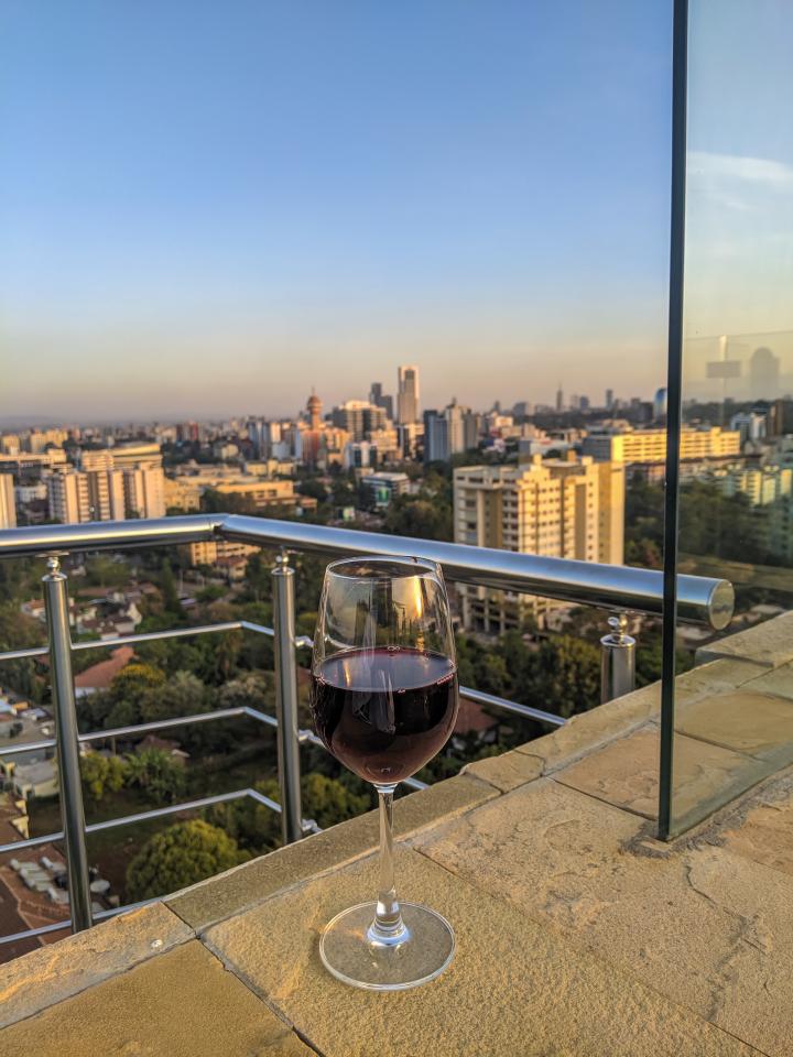 A wine glass on the window sill, looking out from a tall building, with the skyline  in the distance