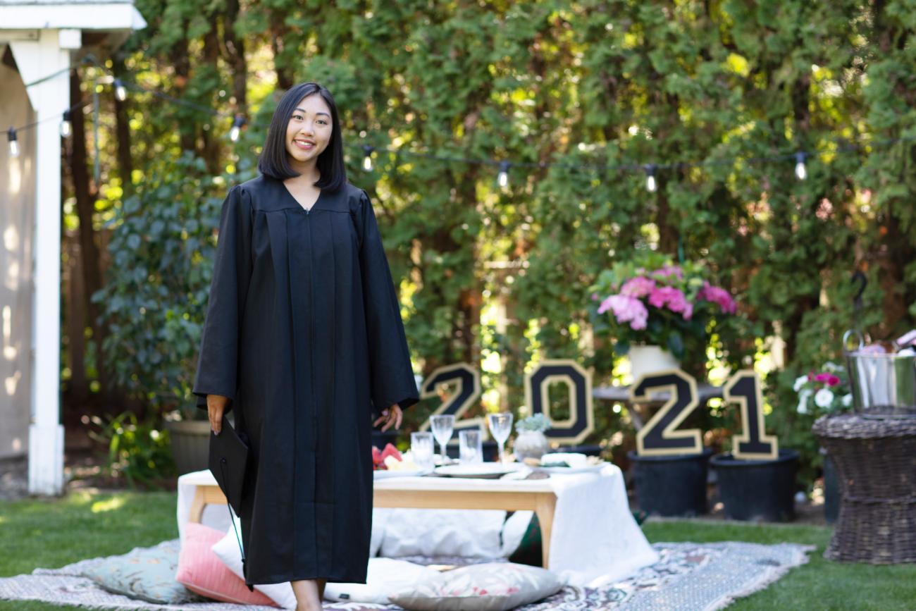 Student in graduation gown at an outdoor celebration with 2021 sign in background