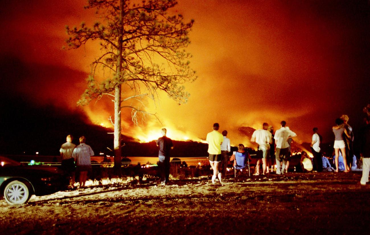 A wide angle image of the backs of a group of people watching a wildfire in the distance