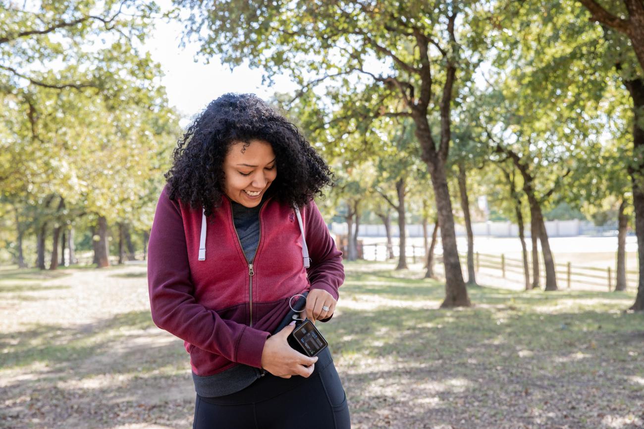 Woman walking in a treed area, looking at her exercise tracker