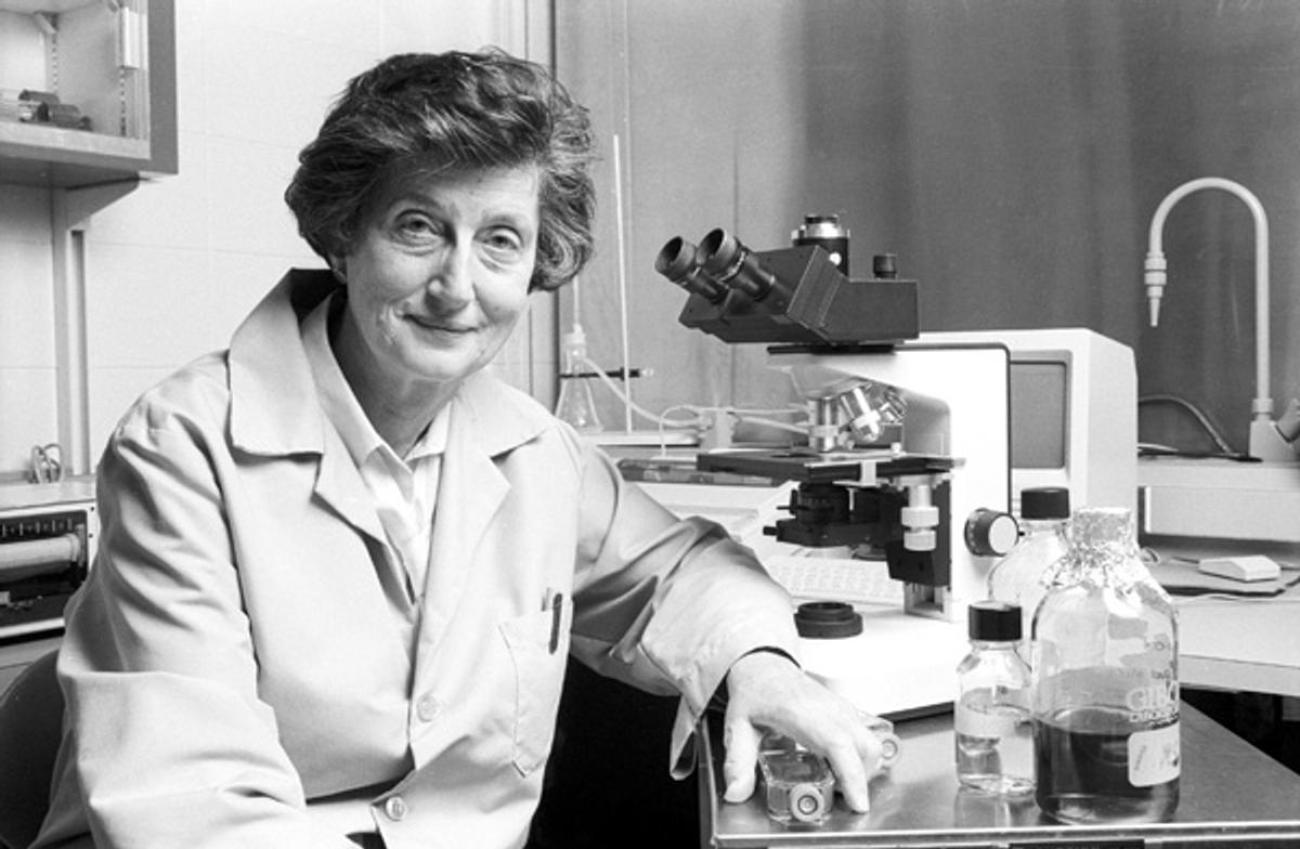 Black and white photo of Dr. Nelly Auersperg seated at a desk with microscope