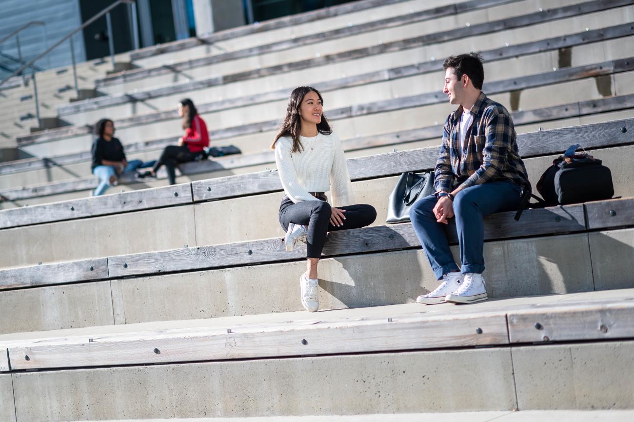 Two young adults chatting and sitting on a set of concrete stairs on a sunny day