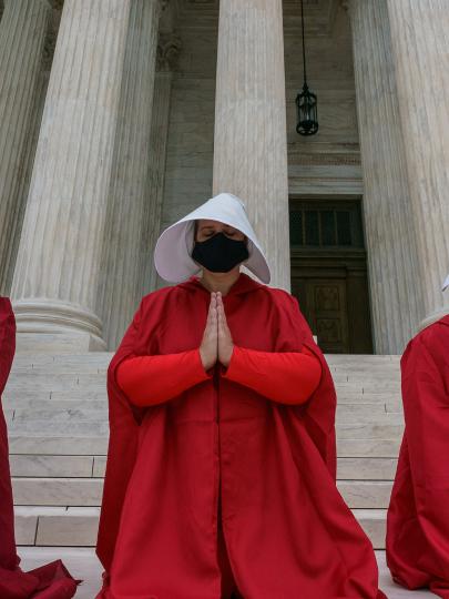 Women in red robes and white bonnets pray on steps in The Handmaid's Tale
