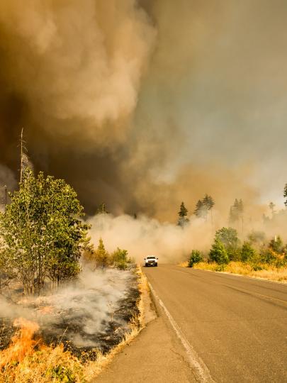 Vehicle drives along highway surrounded by smoke from forest fire