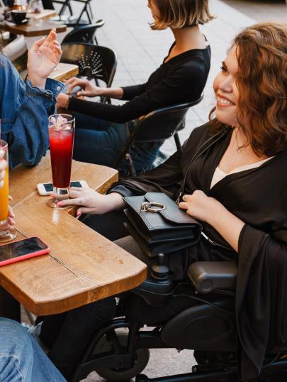 Three female friends with drinks around a table, including one in a wheelchair